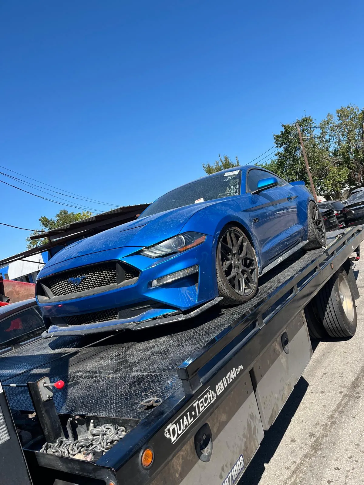 Damaged blue Ford Mustang on flatbed for accident recovery towing in Houston TX
