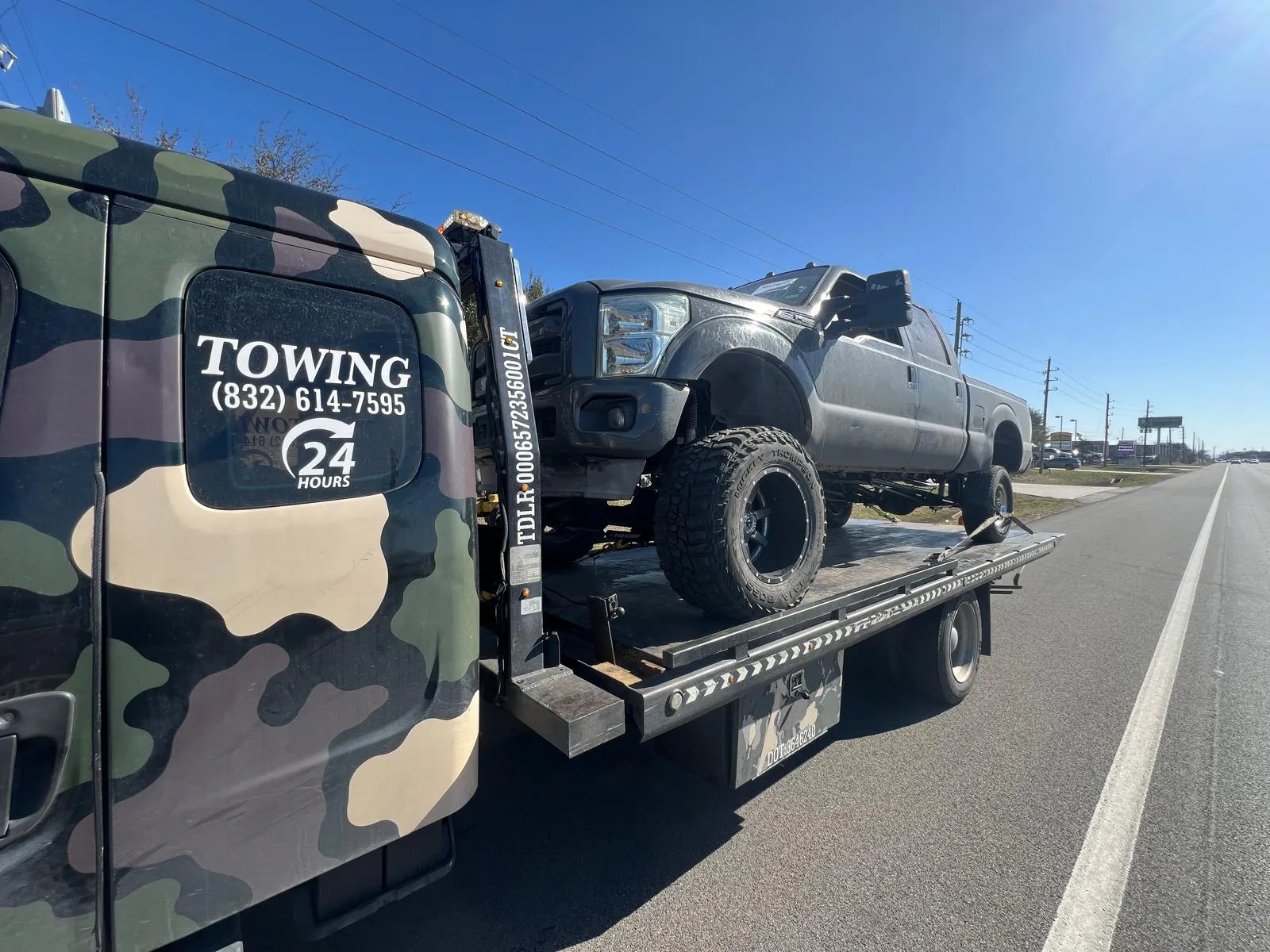 Lifted truck on flatbed tow truck on open highway for long distance towing from Houston TX