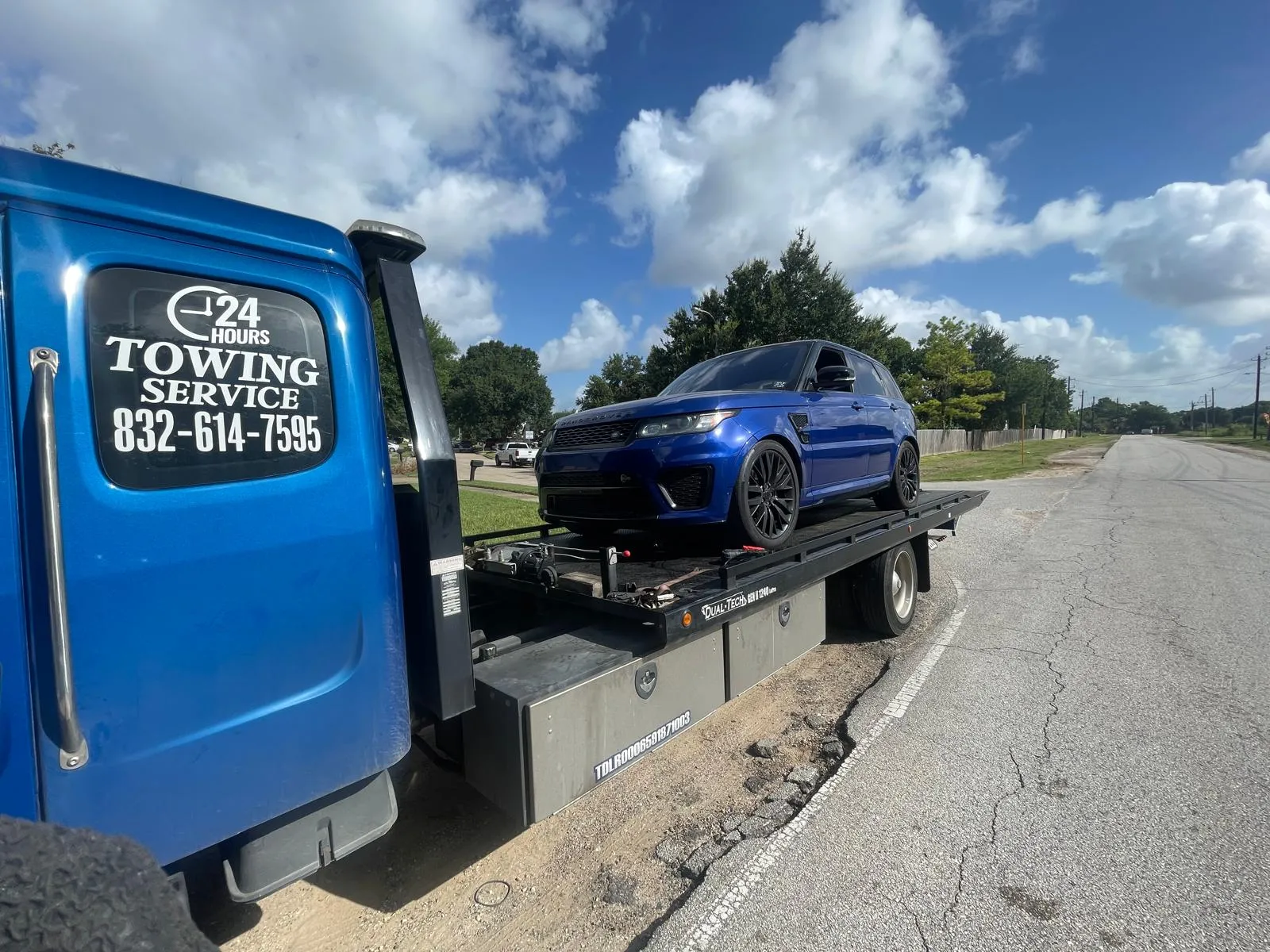 Blue Range Rover Sport on flatbed tow truck on Houston TX road